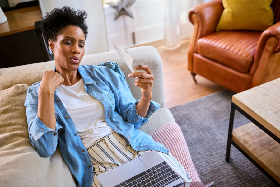 Woman experiencing a hot flash, fanning herself while using a laptop at home.